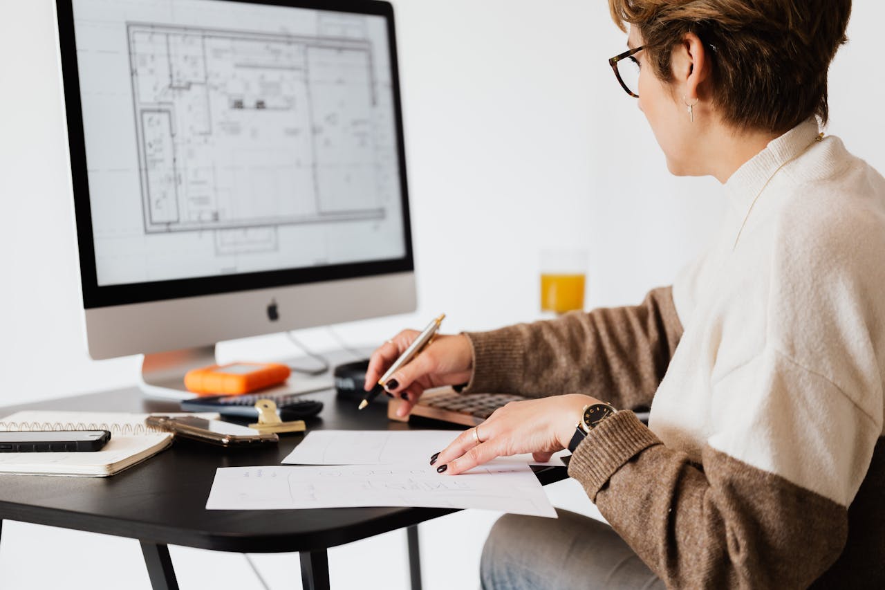who-we-are Woman designing architectural blueprints using desktop computer in a modern office setting.